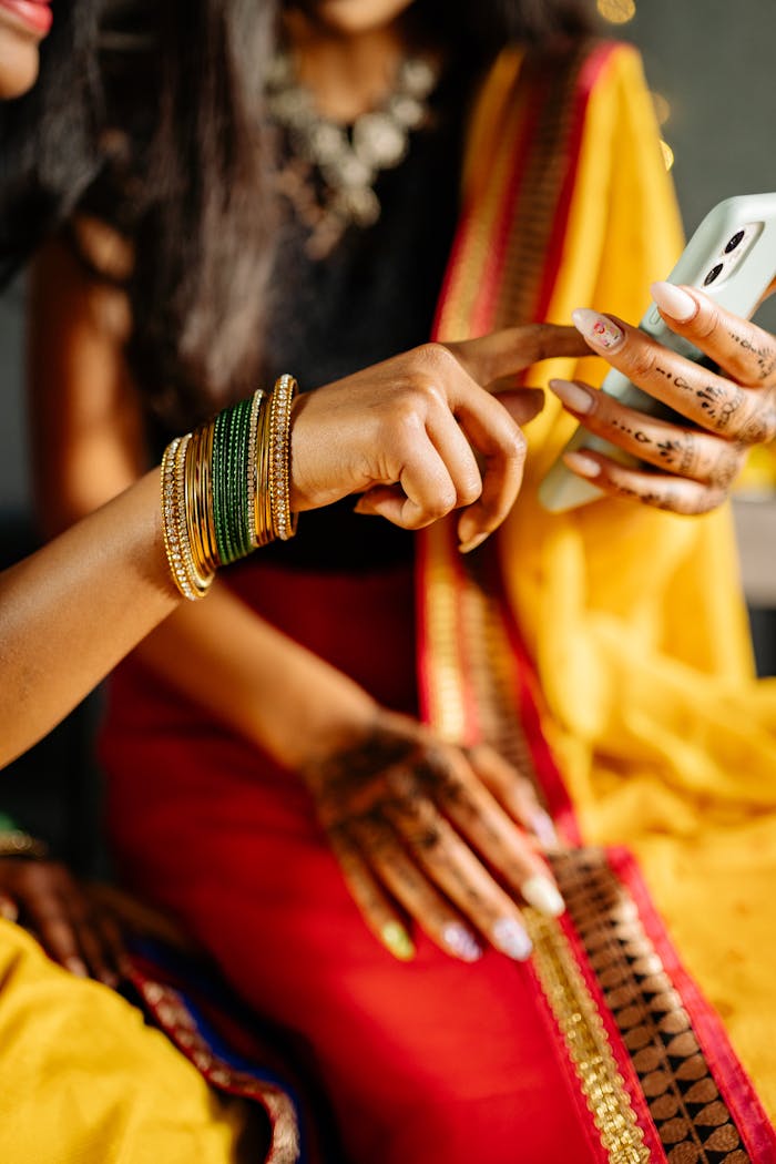 Two women in vibrant traditional sarees engaging with a smartphone, displaying cultural attire and modern technology.